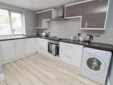 A kitchen with white and grey cabinets a washing machine and appliances on counters at 4 Tyne View in Wark