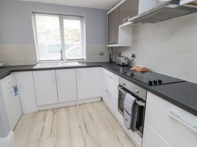A kitchen with white cabinets a black countertop a sink under a window and an oven at 4 Tyne View in Wark