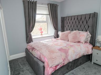 A bedroom with a bed with pink floral bedding and gray upholstered headboard next to a window with gray curtains at 4 Tyne View in Wark