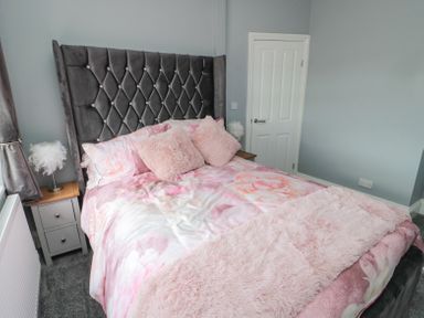 A bedroom with a bed with a high tufted headboard pink bedding and a bedside table with a lamp at 4 Tyne View in Wark