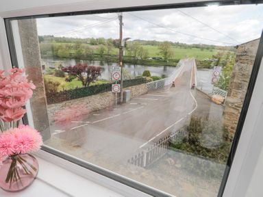View of a road bridge over a river with road signs and green fields in the background seen through a window with pink flowers on the windowsill at 4 Tyne View in Wark