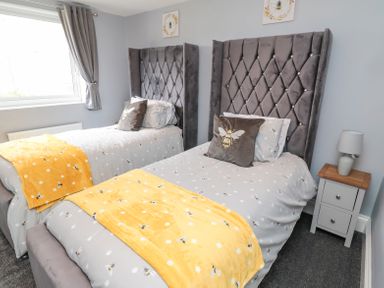 A bedroom with two beds with grey headboards yellow throws and bee themed bedding at 4 Tyne View in Wark