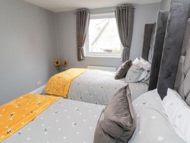 A bedroom with two single beds with patterned bedding and gray curtains at 4 Tyne View in Wark