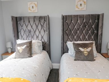 A bedroom with two single beds with grey upholstered headboards and bee-themed bedding at 4 Tyne View in Wark