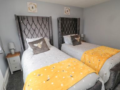 A bedroom with two single beds with gray headboards yellow blankets and bee-themed decor at 4 Tyne View in Wark