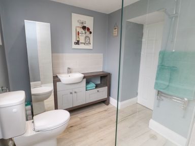 A bathroom with a toilet, sink, vanity unit, full length mirror, shower area with glass partition and towel rail at 4 Tyne View in Wark