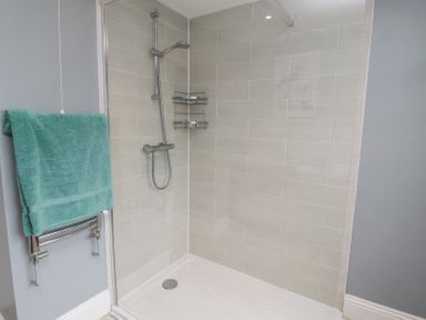 A shower area with a glass panel a wall-mounted shower head and a towel rack with a teal towel at 4 Tyne View in Wark