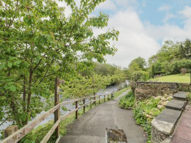 A paved pathway along a river with a wooden fence and greenery at 4 Tyne View in Wark