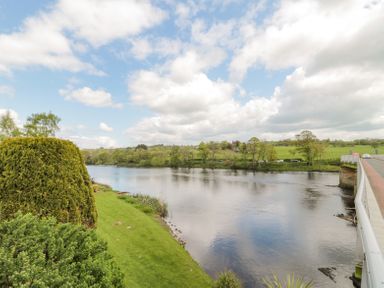 A river with grassy banks and trees next to a bridge at 4 Tyne View in Wark