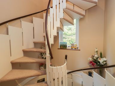A spiral staircase with carpeted steps and white railings near a window with floral decorations at Fellside View in Chapel Stile