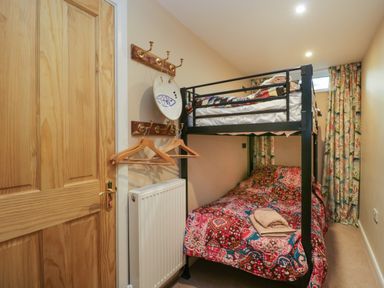 A small bedroom with a bunk bed a wooden door a radiator and hooks with hangers at Fellside View in Chapel Stile