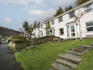 A row of white terraced houses with stone steps leading up a grassy slope at Fellside View in Chapel Stile
