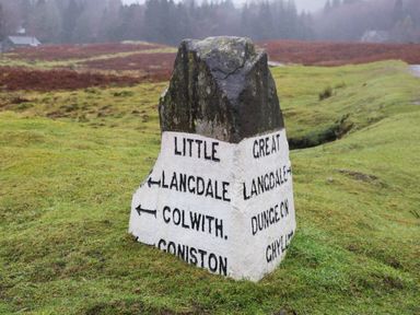 A stone signpost on a grassy field with directions to Little Langdale Colwith Coniston Great Langdale Dungeon Ch Hyde