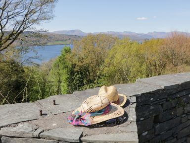 Two straw hats and sunglasses on a stone wall with trees and a lake in the background at Fellside View in Chapel Stile