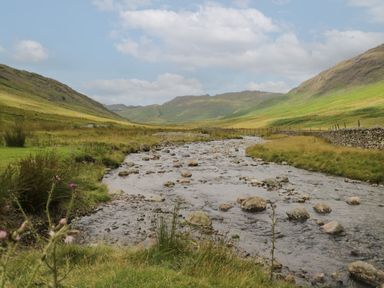 A river flowing through a valley with grassy hills on both sides and a stone wall on the right at Fellside View in Chapel Stile