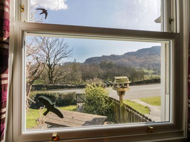 A window looking out to a garden with a bird feeder a wooden table a fence and hills beyond at Fellside View in Chapel Stile