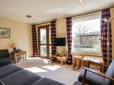 A living room with couch armchairs a small table a wall mounted TV and large windows with curtains at Fellside View in Chapel Stile