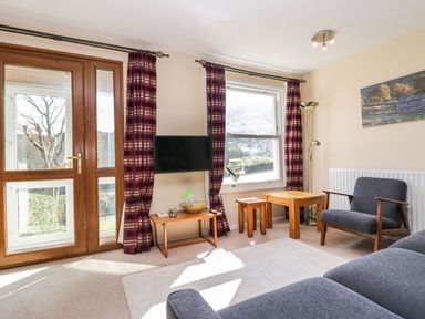 A living room with a sofa armchair wooden tables mounted television and large window at Fellside View in Chapel Stile