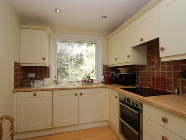 A kitchen with cream cabinets wooden countertops an oven a microwave a toaster a kettle and a window overlooking trees at Fellside View in Chapel Stile