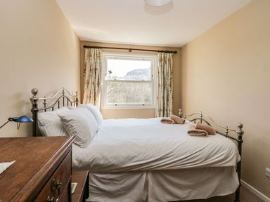 A bedroom with a metal bed frame and white bedding next to a window with floral curtains at Fellside View in Chapel Stile