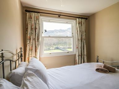 A bedroom with a metal bed frame white bedding floral curtains and a window showing a landscape at Fellside View in Chapel Stile