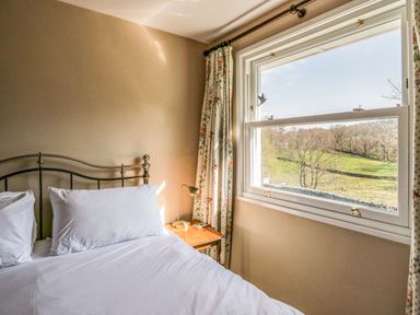 A bedroom with a metal bed frame and white pillows next to a window with floral curtains overlooking a green field at Fellside View in Chapel Stile