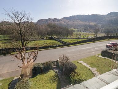 A road with a red car parked beside a grassy yard and stone walls with hills in the background at Fellside View in Chapel Stile