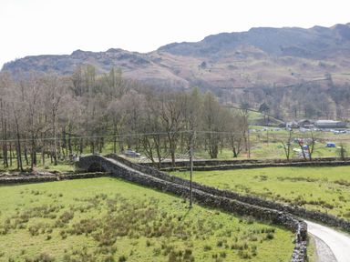 A rural landscape with a stone bridge over a narrow road surrounded by green fields and hills at Fellside View in Chapel Stile