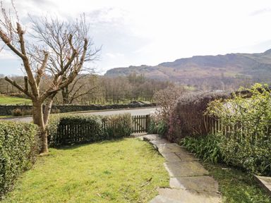 A garden with a stone pathway trees bushes and a wooden gate with hills in the background at Fellside View in Chapel Stile