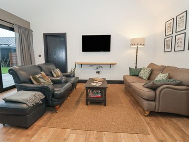 A living room with two sofas a coffee table a floor lamp and a wall-mounted television at Skylark in Bishop Wilton