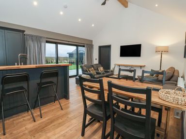 An open plan living room with a dining table and chairs a kitchen island bar with stools sliding glass doors and couches at Skylark in Bishop Wilton