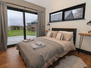 A bedroom with a bed with pillows and towels near a sliding glass door and windows at Skylark in Bishop Wilton