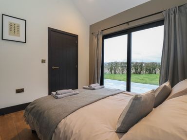 A bedroom with a bed and folded towels near a sliding glass door overlooking a garden at Skylark in Bishop Wilton