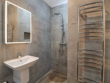 A bathroom with a wall-mounted sink shower area heated towel rail and illuminated mirror at Skylark in Bishop Wilton