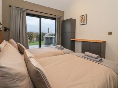 A bedroom with two beds and towels on them a cabinet and dresser with a wooden top and a sliding glass door leading outside at Skylark in Bishop Wilton