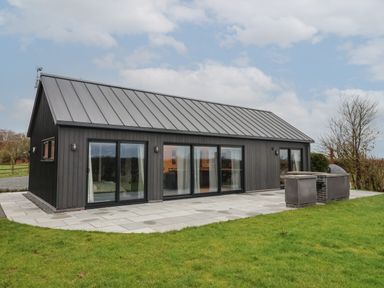 A single story building with large glass sliding doors on a paved patio with a built in grill on grass outside Skylark in Bishop Wilton