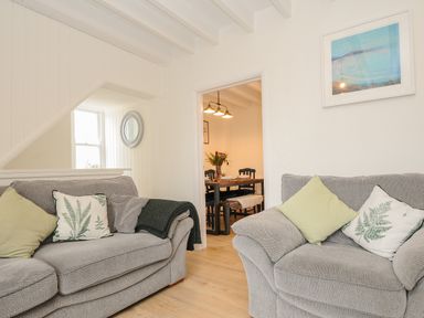 A living room with two gray sofas with green and white pillows and a view into a dining area at Carvannel Cottages North Cliffs near Portreath