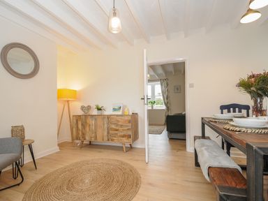 A dining room with a wooden sideboard a floor lamp a round rug and a wooden dining table with dishes at Carvannel Cottages North Cliffs near Portreath