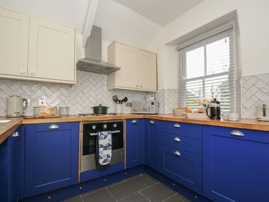 A kitchen with blue and white cabinets a stove a microwave and a window with blinds at Carvannel Cottages North Cliffs near Portreath