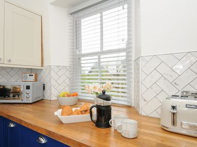 A kitchen countertop with a toaster, coffee press, two mugs, croissants, a fruit bowl and a radio at Carvannel Cottages in North Cliffs near Portreath