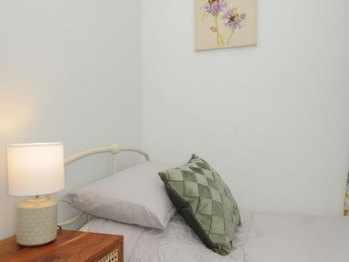 A bed with grey bedding and green cushion next to a wooden nightstand with a table lamp at Carvannel Cottages North Cliffs near Portreath