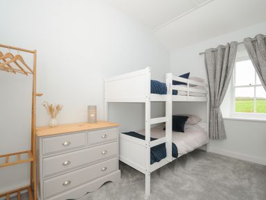 A bedroom with white bunk beds a gray chest of drawers and a wooden clothes rack at Carvannel Cottages in North Cliffs near Portreath