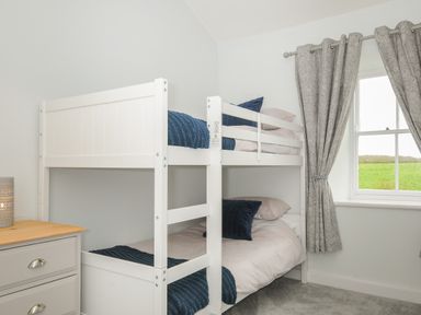 A bedroom with white bunk beds next to a window with patterned curtains at Carvannel Cottages North Cliffs near Portreath