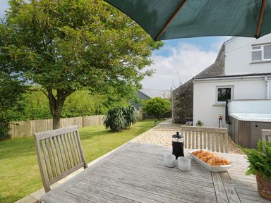An outdoor wooden table with croissants mugs and a coffee press under an umbrella next to a garden and a house at Carvannel Cottages North Cliffs near Portreath
