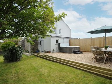 An outdoor area with a house, a hot tub, a table with chairs and an umbrella, and a grassy lawn at Carvannel Cottages North Cliffs near Portreath