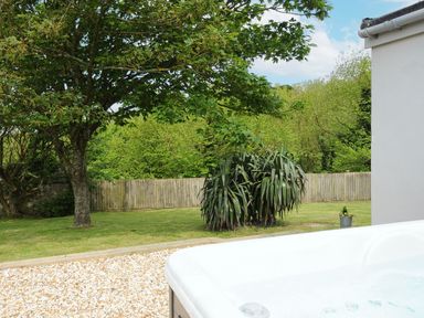 A backyard with a tree a fence green grass and a hot tub at Carvannel Cottages North Cliffs near Portreath