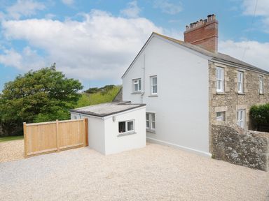 Exterior of a semi detached stone and white house with gravel driveway and wooden gate at Carvannel Cottages North Cliffs near Portreath