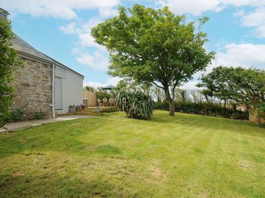 A garden with mown grass a tree and patio furniture beside a stone and white house at Carvannel Cottages in North Cliffs near Portreath