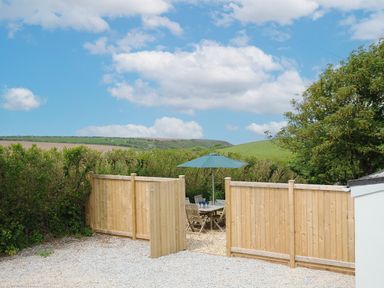A garden area with wooden fence and patio furniture with umbrella at Carvannel Cottages North Cliffs near Portreath