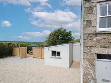 A gravel yard with a small white building and wooden fenced seating area at Carvannel Cottages in North Cliffs near Portreath